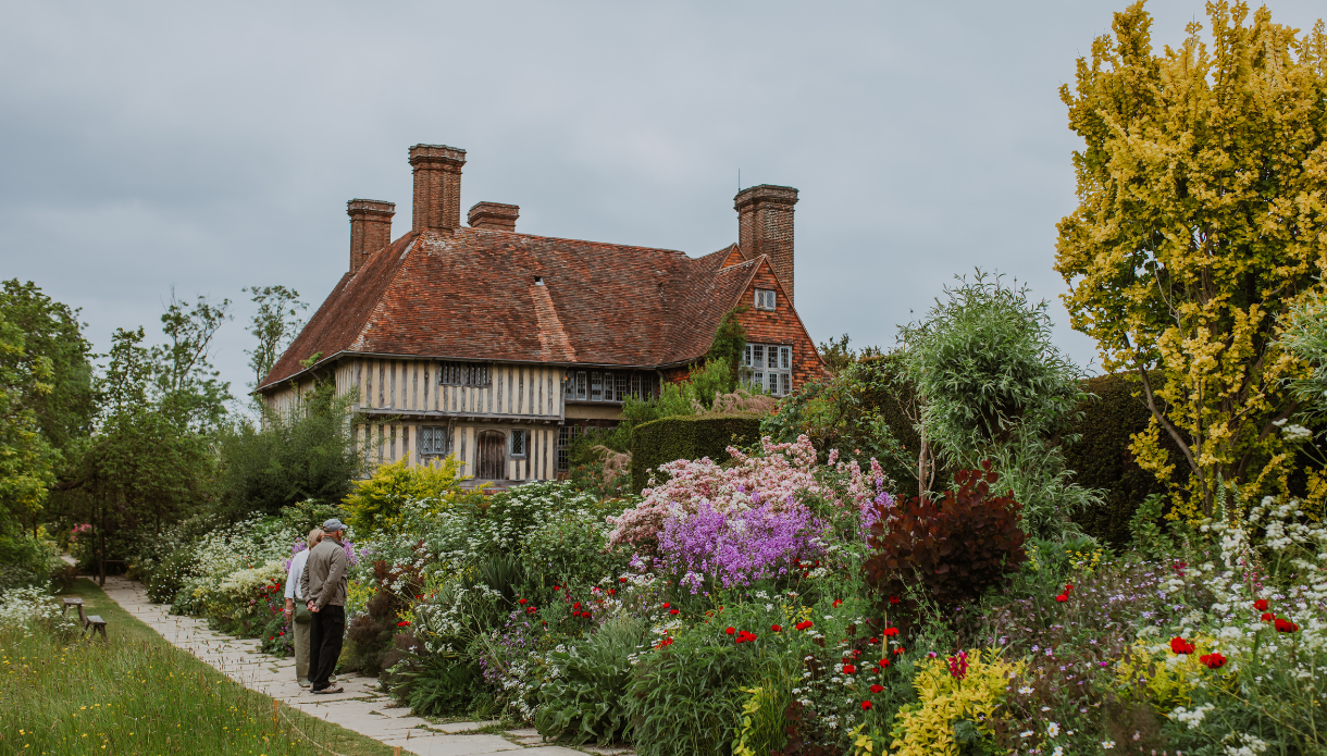 Historic Great Dixter house behind vibrant flower-filled garden with a person walking along the path.